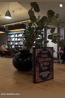 photograph of a copy of These Dreaming Spires, edited by Marie O'Regan and Paul Kane, standing on a wooden surface in front of a dark round vase, with a plant overhanging the book