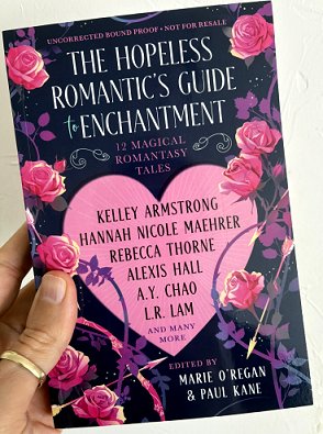 photograph of a man's hand holding a copy of The Hopeless Romantic's Guide to Enchantment, edited by Marie O'Regan and Paul Kane, up against a white background