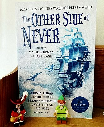 photograph of a copy of The Other Side of Never, edited by Marie O'Regan and Paul Kane, standing on a wooden surface, with Lego figures of Captain Hook and Peter Pan