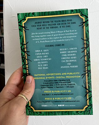 photograph of a man's hand holding a copy of Land of Oz, edited by Marie O'Regan and Paul Kane, up against a white background to show the book's back cover