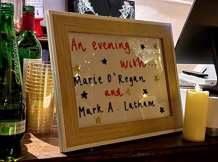 handwritten sign in a wooden frame. Text reads: An evening with Marie O'Regan and Mark A. Latham