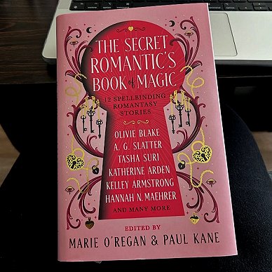 photograph of a copy of The Secret Romantic's Book of Magic, edited by Marie O'Regan and Paul Kane, on a deak - leaning against a laptop keyboard