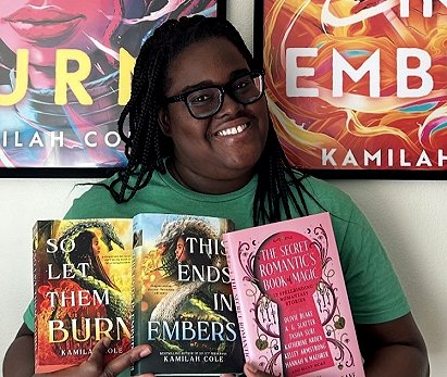 photograph of a smiling Kamilah Cole holding copies of her novels So Let Them Burn and This Ends in Embers, alongside a copy of The Secret Romantic's Book of Magic, edited by Marie O'Regan and Paul Kane