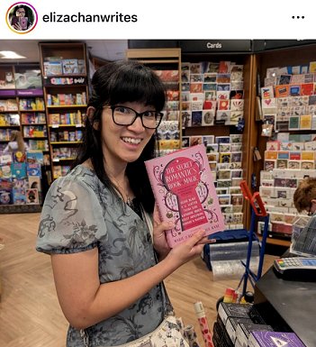photograph of a smiling Eliza Chan in a bookshop, holding up a copy of The Secret Romantic's Book of Magic, edited by Marie O'Regan and Paul Kane